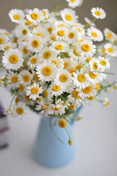 a blue vase filled with lots of white and yellow flowers on top of a table