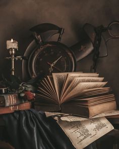 an open book sitting on top of a pile of books next to a candle and clock