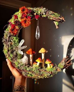 a person holding up a wreath with mushrooms and flowers on it