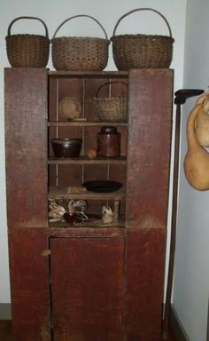 an old wooden cabinet with baskets and other items on it's top shelf in a room