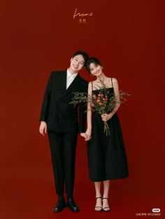 two people standing next to each other in front of a red wall with flowers on it