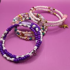 three bracelets with beads and charms on a pink surface, one has a star charm