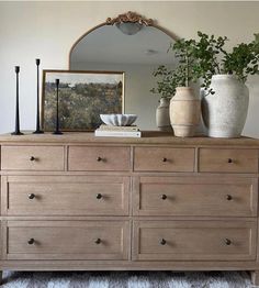 a dresser with two vases on top of it and a mirror in the background