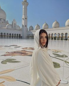 a woman in a white dress standing in front of a building with arches and pillars