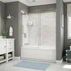 a bathroom with gray walls and white fixtures, including a bathtub that has a glass shower door