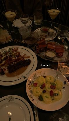 a table topped with plates filled with food and glasses on top of each other next to wine glasses