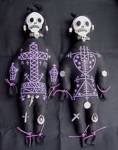 two black cloth dolls with purple and white designs on them, sitting next to each other