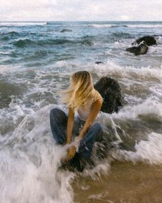 a woman sitting on top of a rock in the ocean next to rocks and water