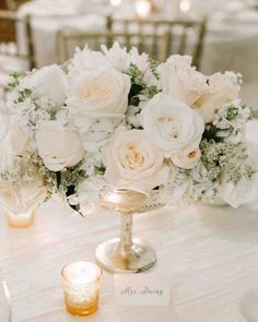 the centerpieces on this table are all white and have flowers in them, along with candles