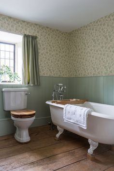 an old fashioned bathtub and toilet in a bathroom with green wallpaper on the walls