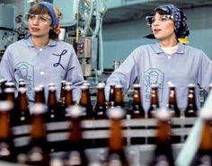 two women standing in front of rows of beer bottles with writing on their shirts and glasses