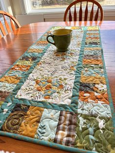 a wooden table with a green cup on it and a quilted placemat sitting on top of it