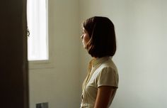 a woman standing in front of a window looking out at the outside world with her hands on her hips