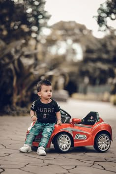 a little boy sitting on top of a red toy car