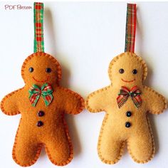 two ornaments made to look like gingerbreads hanging from strings on a white surface