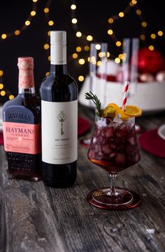 two bottles of booze sit on a table next to a glass with ice and lemon wedges