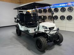 a white golf cart parked in front of a wall with tires and wheels on it