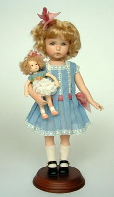 a doll is holding a teddy bear on a wooden stand with a white wall in the background