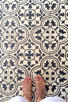 a person's feet with red nail polish standing in front of a black and white tile floor