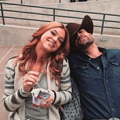 a man and woman sitting next to each other on a bench with drinks in their hands