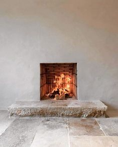 a fireplace in a white walled room with stone flooring and a lit fire place