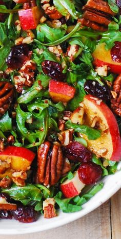 a salad with apples, cranberries and pecans in it on a white plate