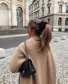 a woman walking down a cobblestone street carrying a black handbag on her shoulder