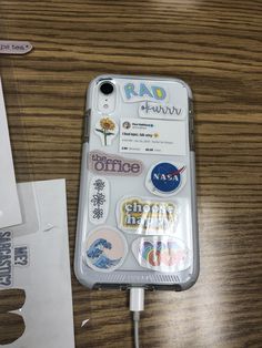 an iphone case with stickers on it sitting next to a charger and paper