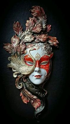 a white mask with red and gold leaves on it's face, against a black background