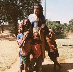 a woman standing next to four children in front of a tree and dirt ground area