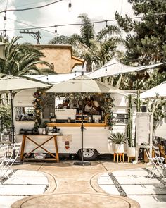 an outdoor food cart with umbrellas and chairs on the ground in front of palm trees