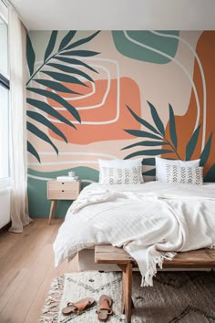 a bedroom with an orange and green mural on the wall, white bedding and wooden flooring