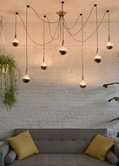 a grey couch with yellow pillows and hanging lights