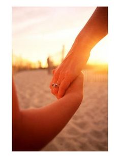 a person holding the hand of another persons hand at sunset or sunrise on the beach