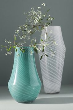 two vases with white flowers in them on a gray surface, one has green stems and the other is blue