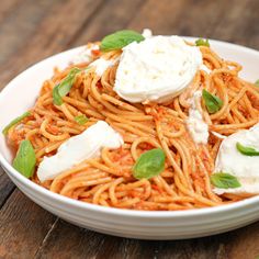 a white bowl filled with pasta and cheese on top of a wooden table next to green leaves