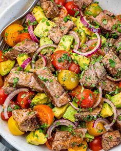 a white bowl filled with meat, tomatoes and onions on top of a wooden table