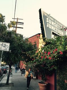 a woman is walking down the sidewalk in front of a sign that says sunset junction