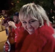 a woman in red shirt holding up a beer bottle with mouth open and tongue out