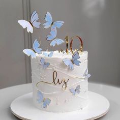 a white cake with blue butterflies on it and the word love spelled in gold letters