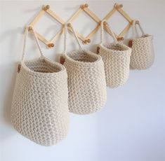 three crocheted baskets hanging on a wall with wooden pegs attached to them