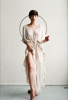 a woman in a white dress with a hoop around her neck and legs, standing on the floor