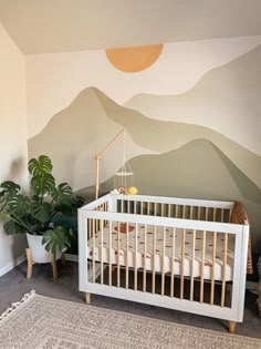 a baby's room with mountains painted on the wall and a white crib