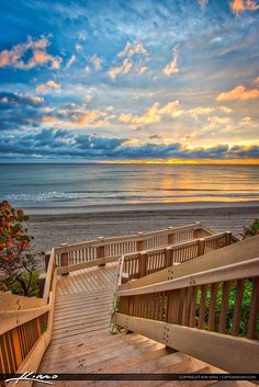 stairs lead down to the beach as the sun sets over the ocean in the background