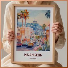 a woman holding up a framed poster with the los angeles sign in front of her