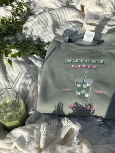 a sweatshirt sitting on top of a bed next to a jar of green liquid and a plant