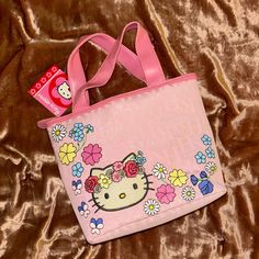 a hello kitty bag with flowers on it sitting on a brown velvet bed sheet, next to a hello kitty sticker