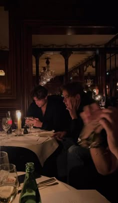 three people sitting at a table in a restaurant with wine glasses and candles on it