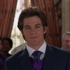 a man in a suit and tie looking at the camera with other people behind him