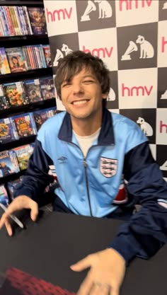 a young man sitting at a table in front of a display of video game dvds